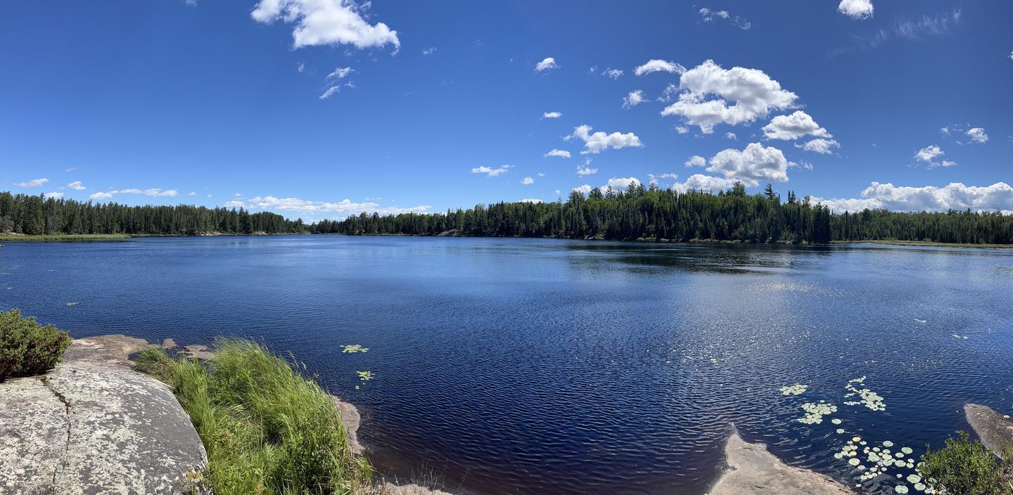 Panoramic view of a vast lake surrounded by green forest under a blue sky.