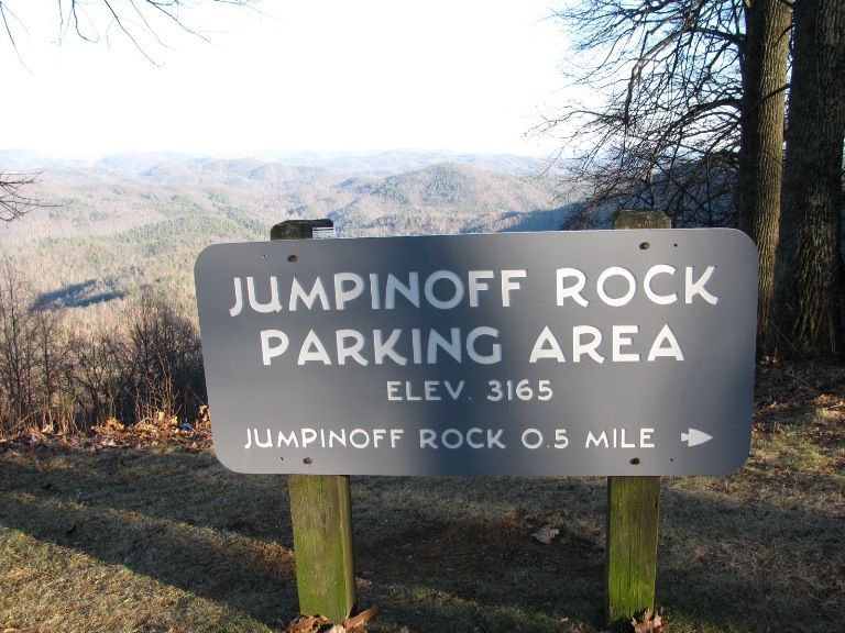 A dark sign on wooden posts, with distant mountains and bare trees. - Jumpinoff Rock Trail
