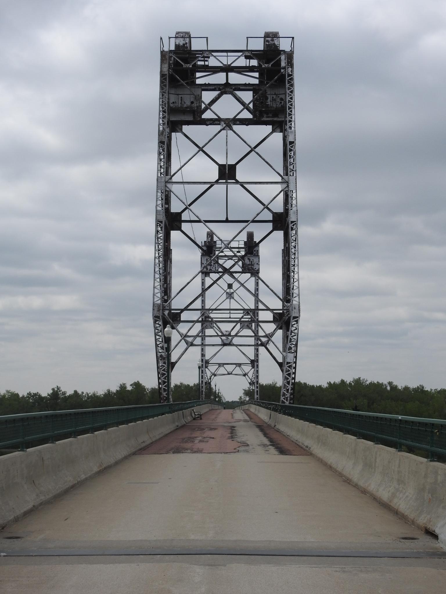 Tall metal bridge tower over a concrete road under an overcast sky.