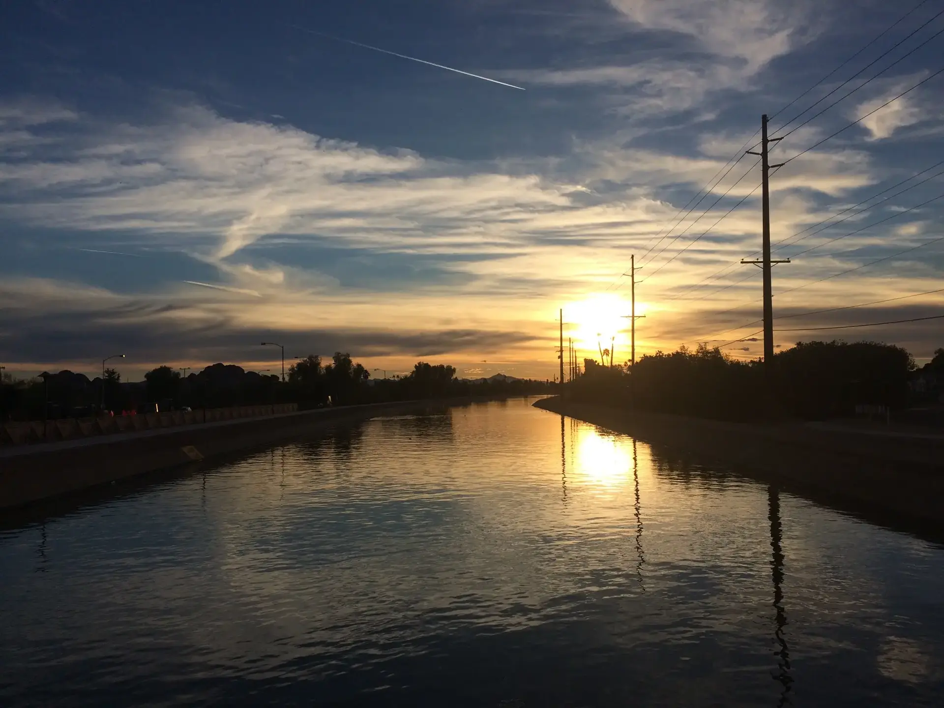A canal reflects a vibrant sunset sky with silhouetted power lines.