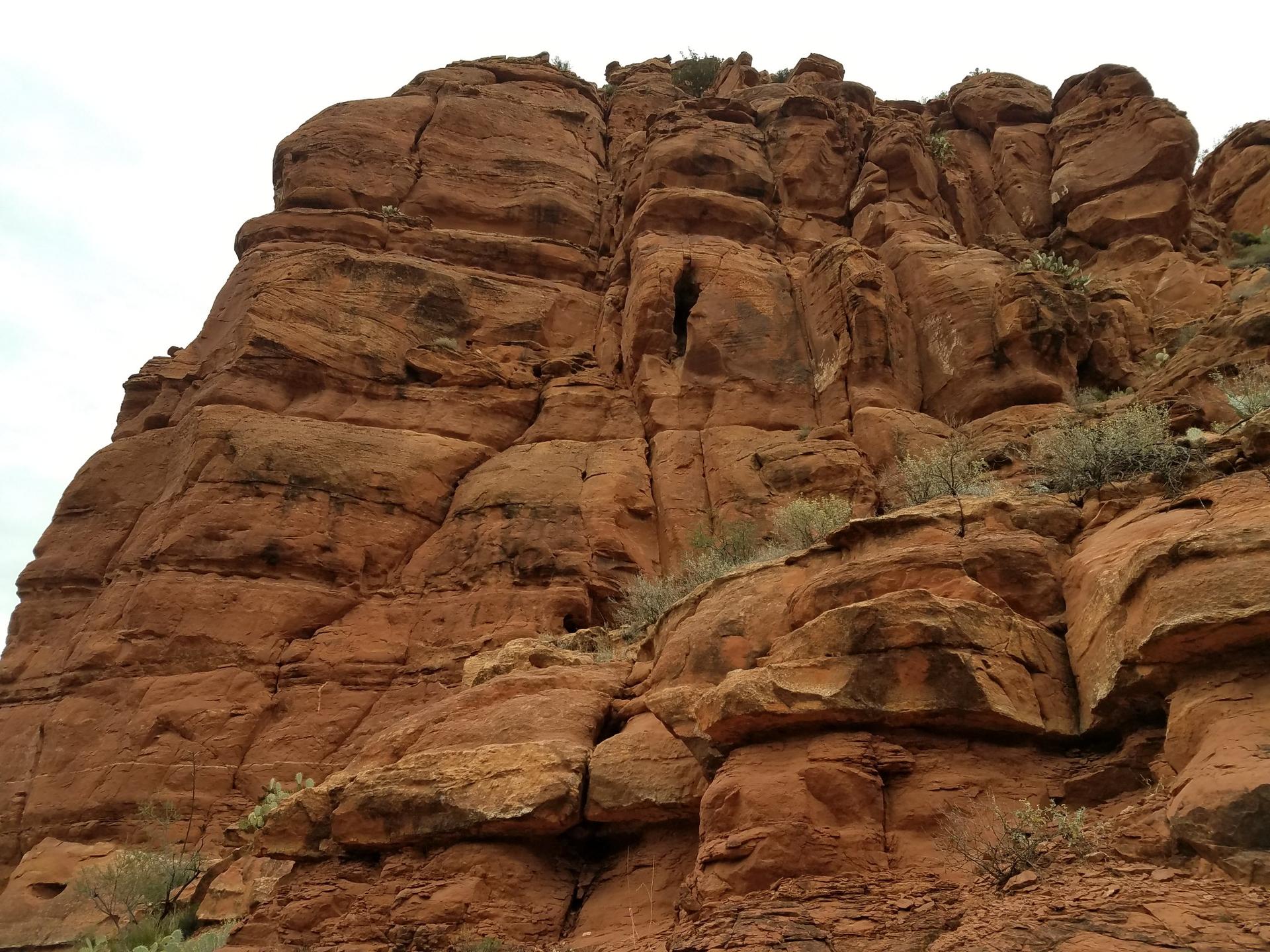A towering, textured red rock cliff under an overcast sky.