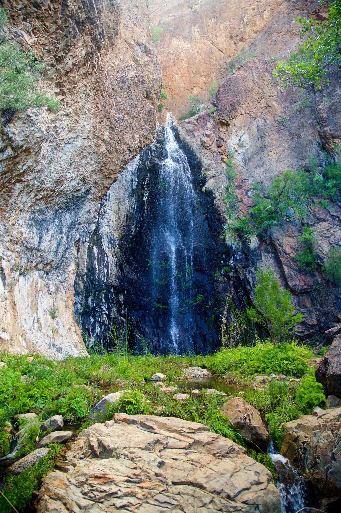 A tall waterfall cascades down a rocky cliff into a lush green pool.