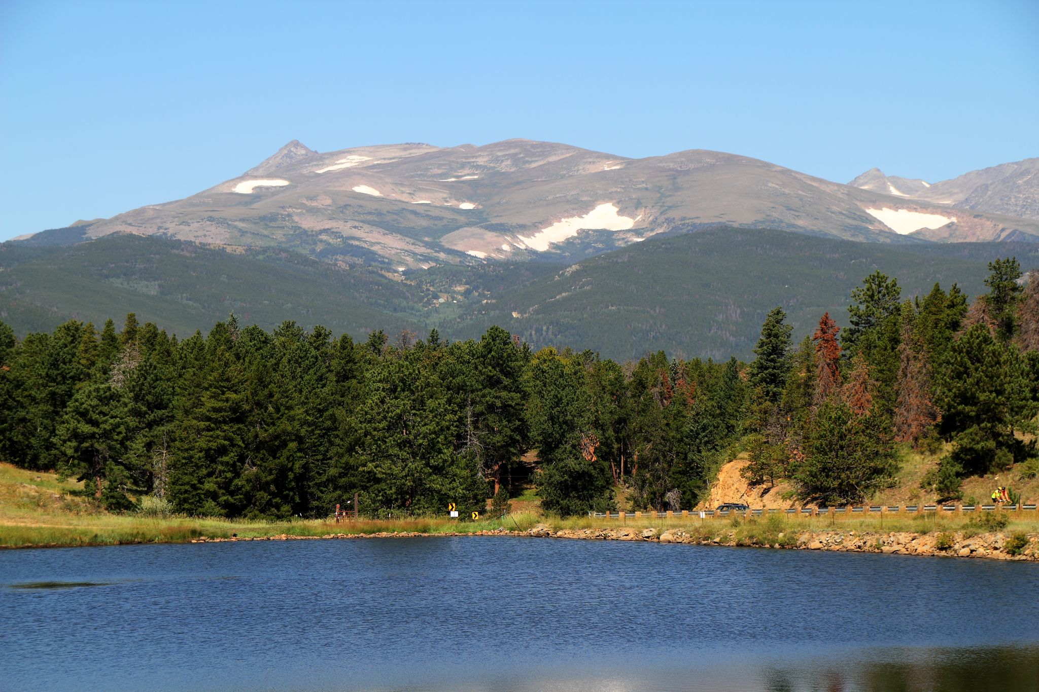 A serene lake with a pine forest and snow-capped mountains under clear skies. - Rollinsville & Barker Reservoir loop from Nederland