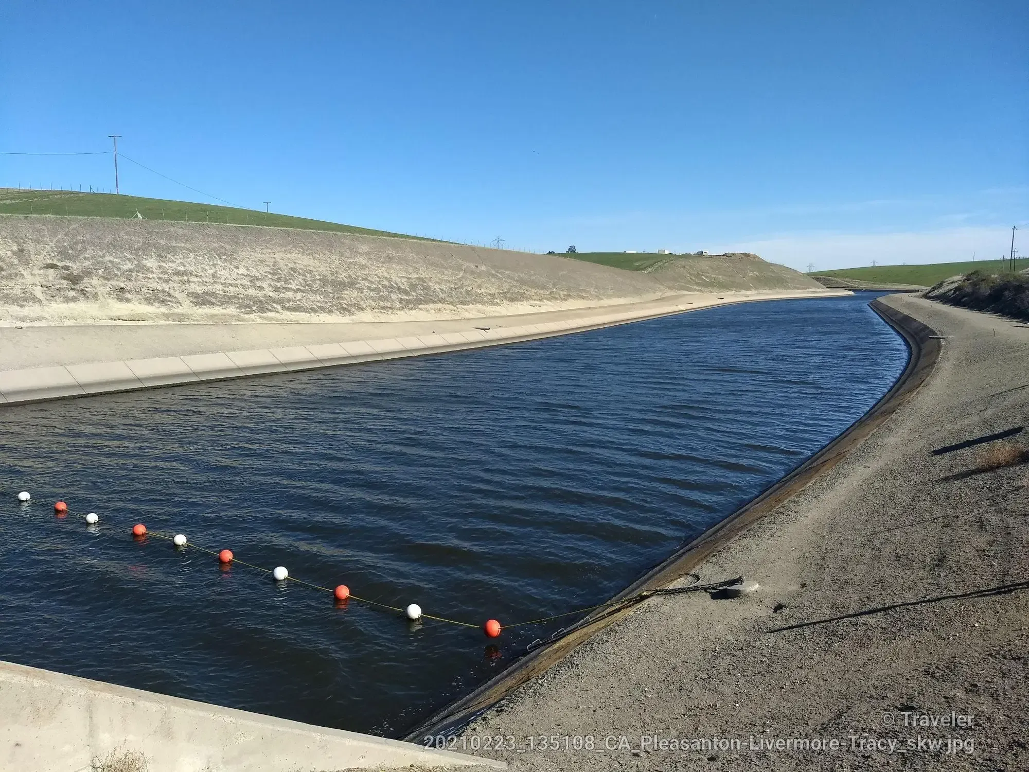 Wide concrete canal with dark water, grassy banks, under a clear sky. - Livermore Century Ride