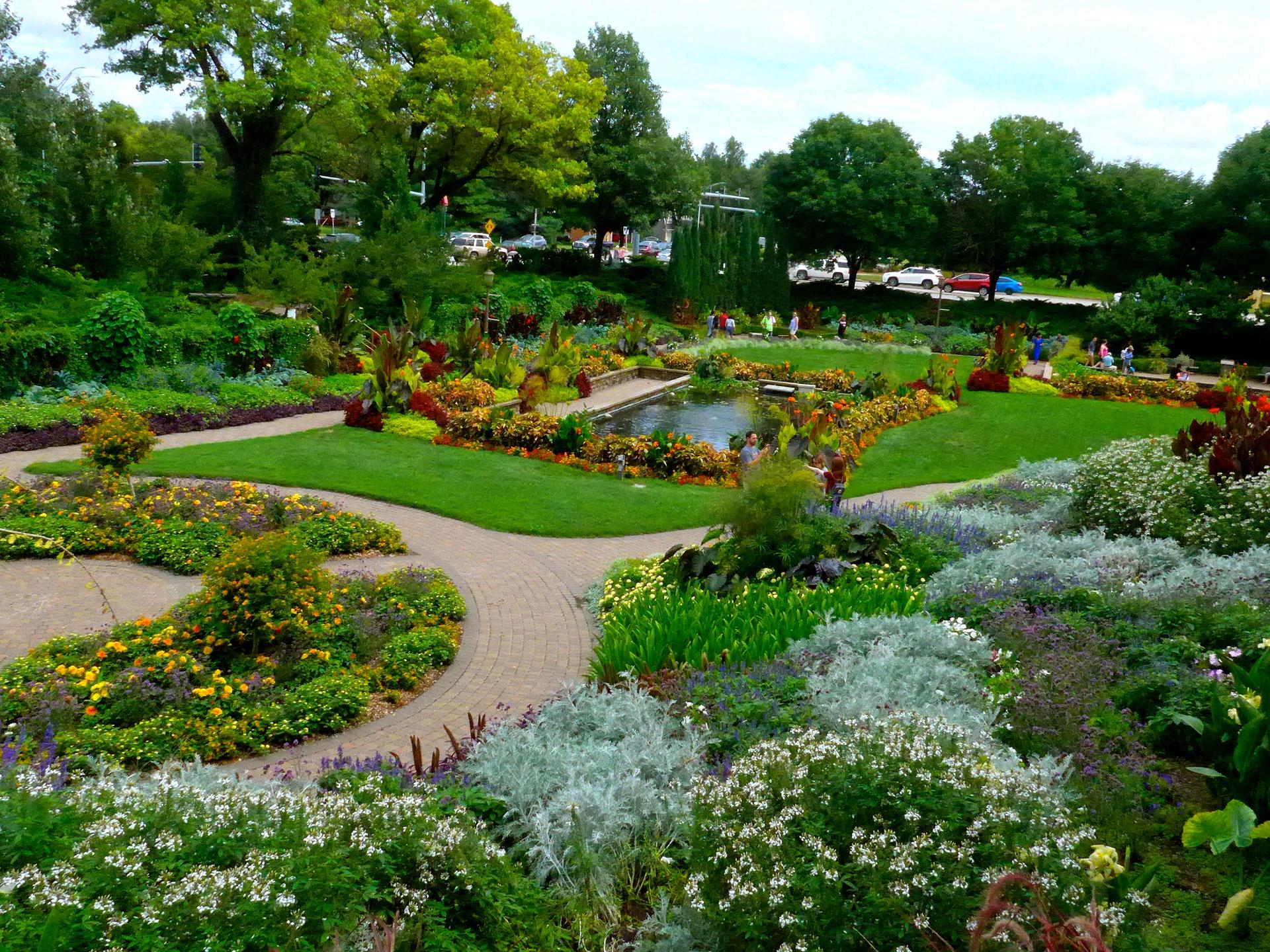 A vibrant, manicured garden with a pond, diverse plants, and distant people.