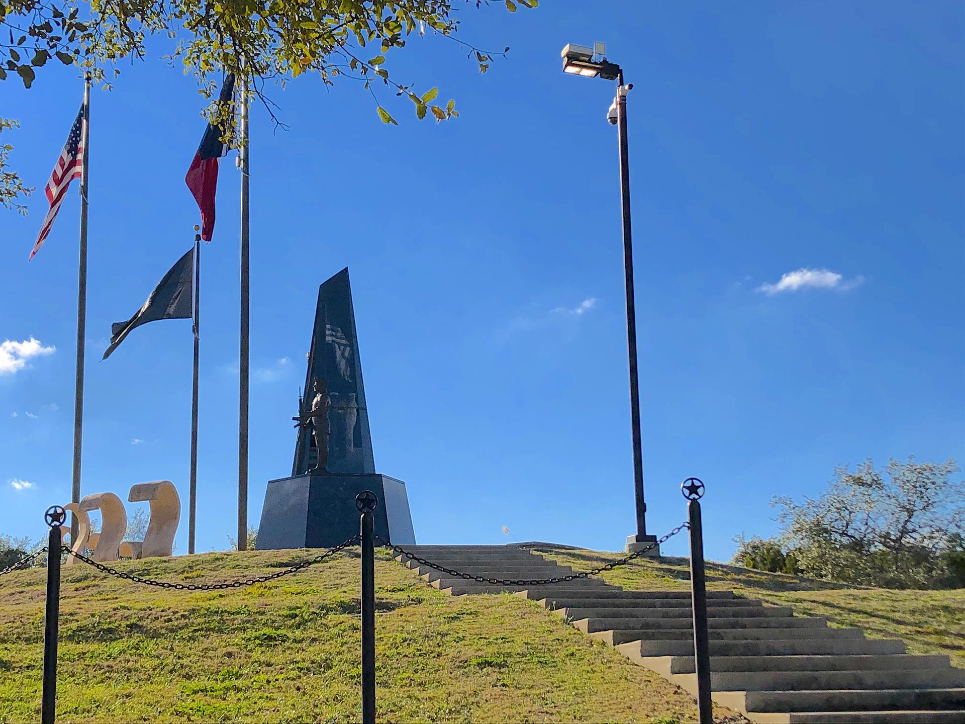 Monument with flags on a grassy hill under a bright blue sky.