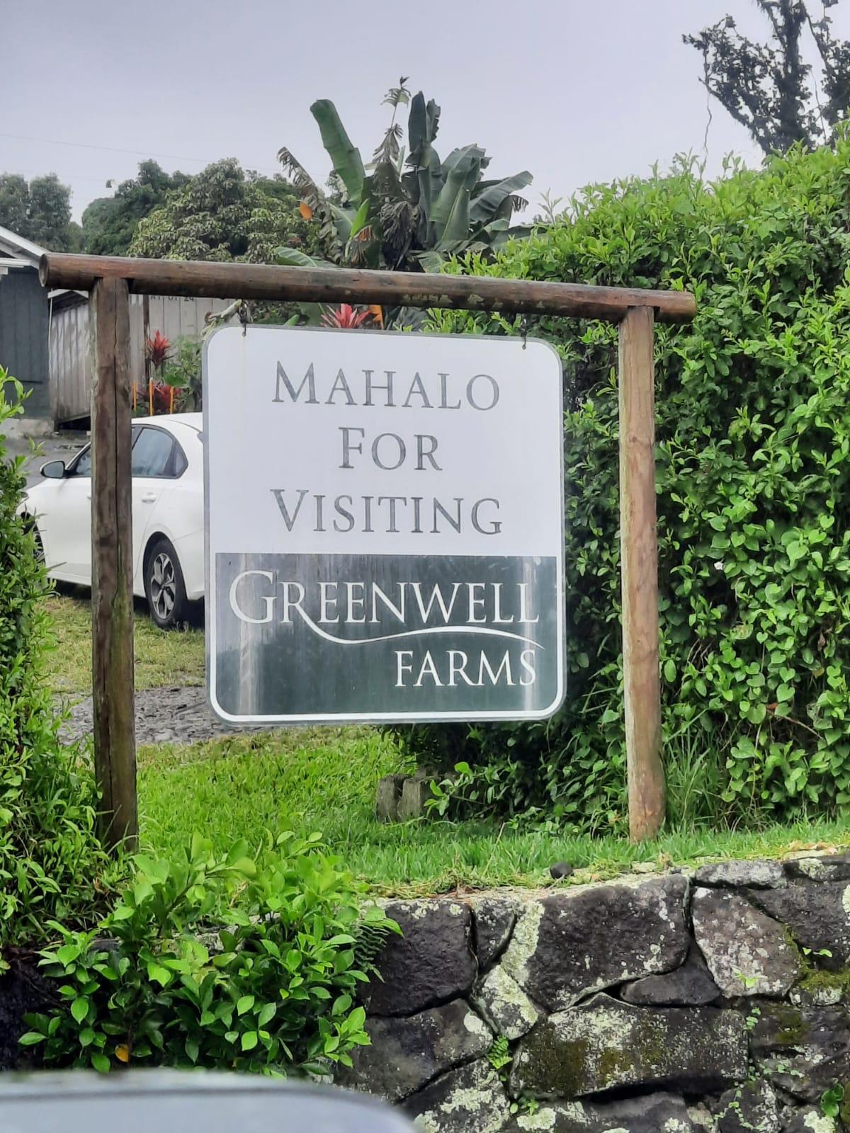 A white sign on a wooden frame, surrounded by lush green foliage under an overcast sky.