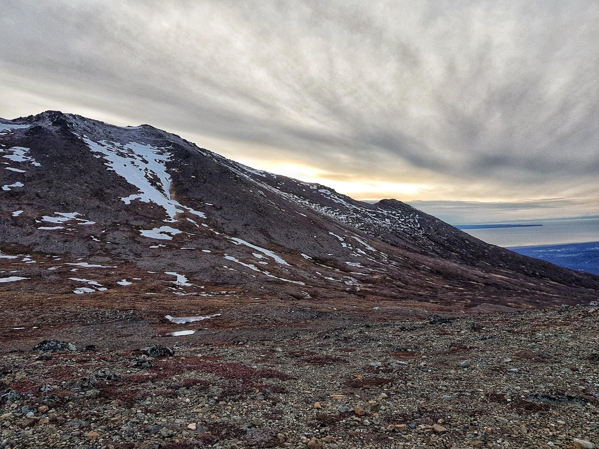 Barren mountain landscape with snow, cloudy sky, and distant water at sunset. - Wolverine Peak via Basher Trail