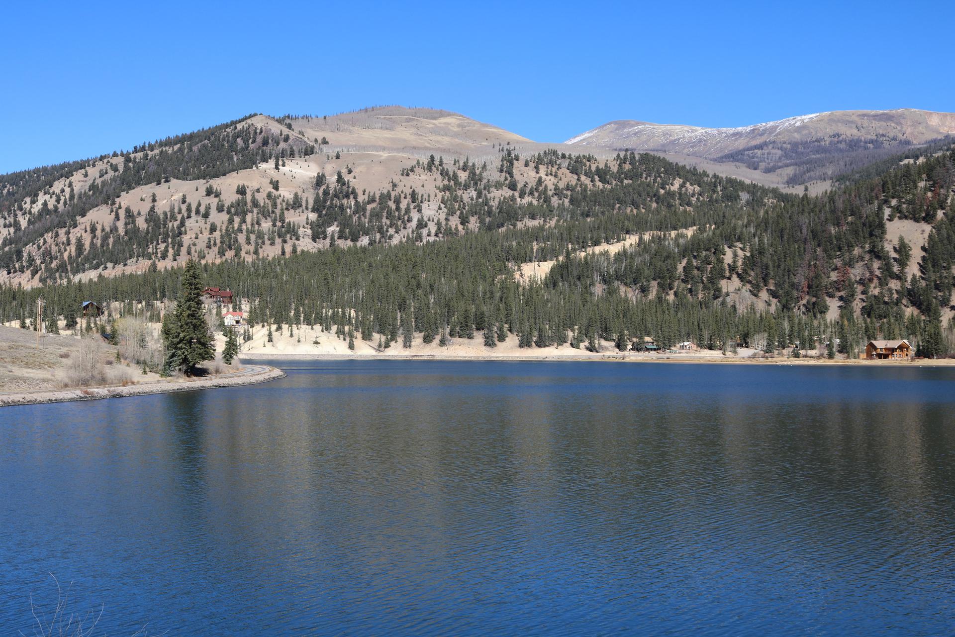Serene lake surrounded by pine-covered mountains under a clear blue sky.