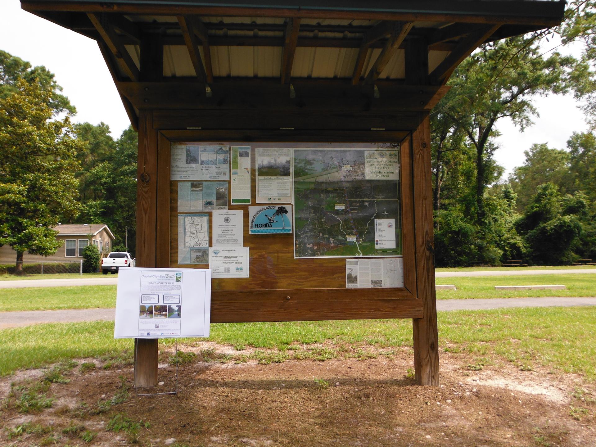 A wooden information kiosk with a map and papers under a bright sky.