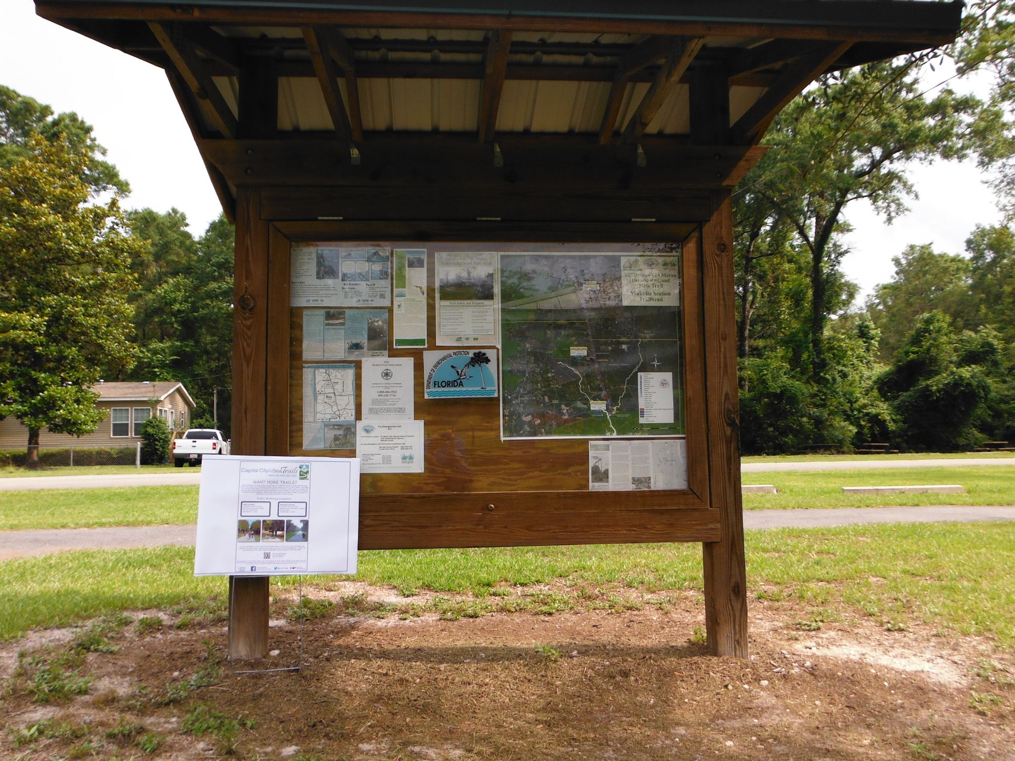 A wooden information kiosk with a map and papers under a bright sky. - Tallahassee-St. Marks Historic Railroad State Trail