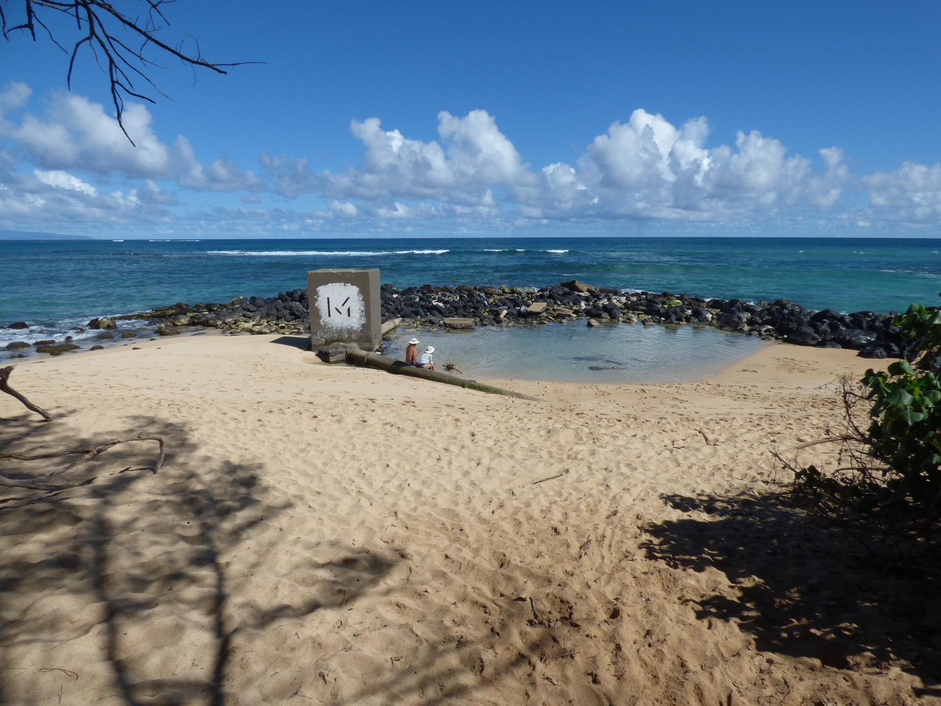 Bright beach scene with a concrete marker, calm tidal pool, and ocean.