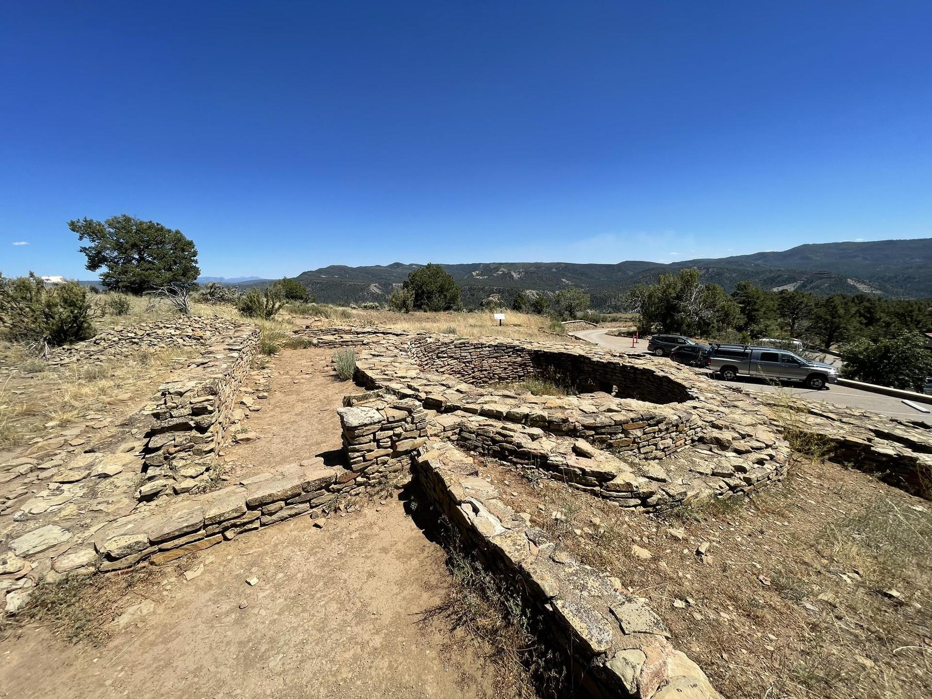 Ancient stone ruins with circular structures on a sunny, dry hilltop.