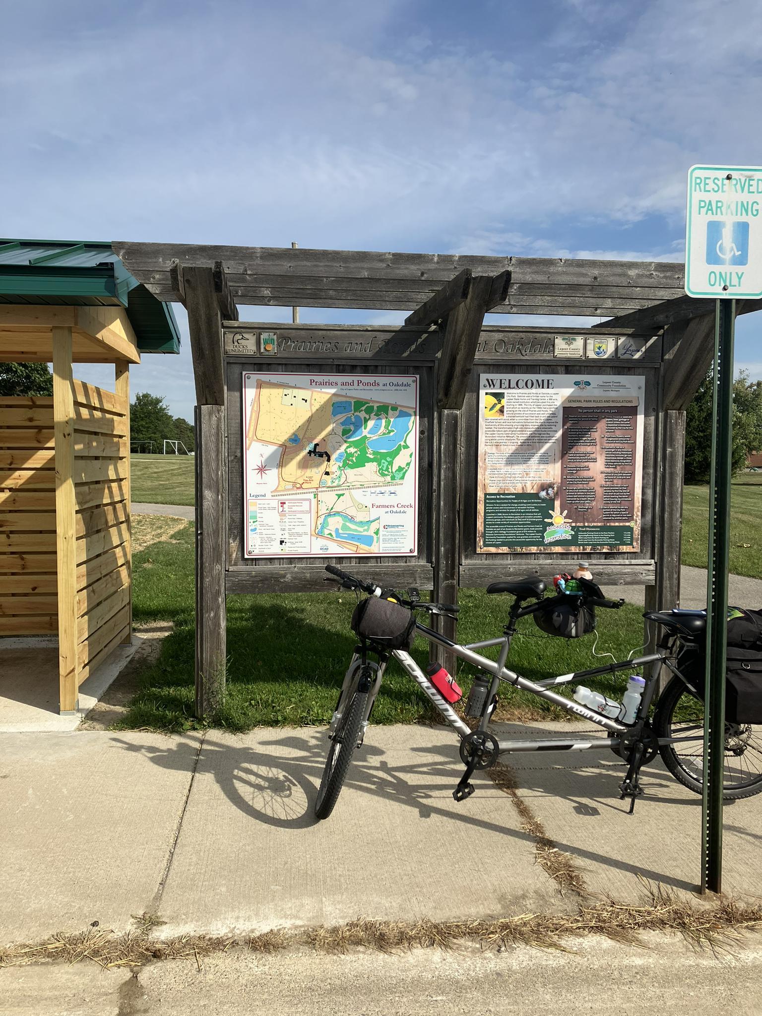 A bicycle parked on a paved path next to an outdoor information board.