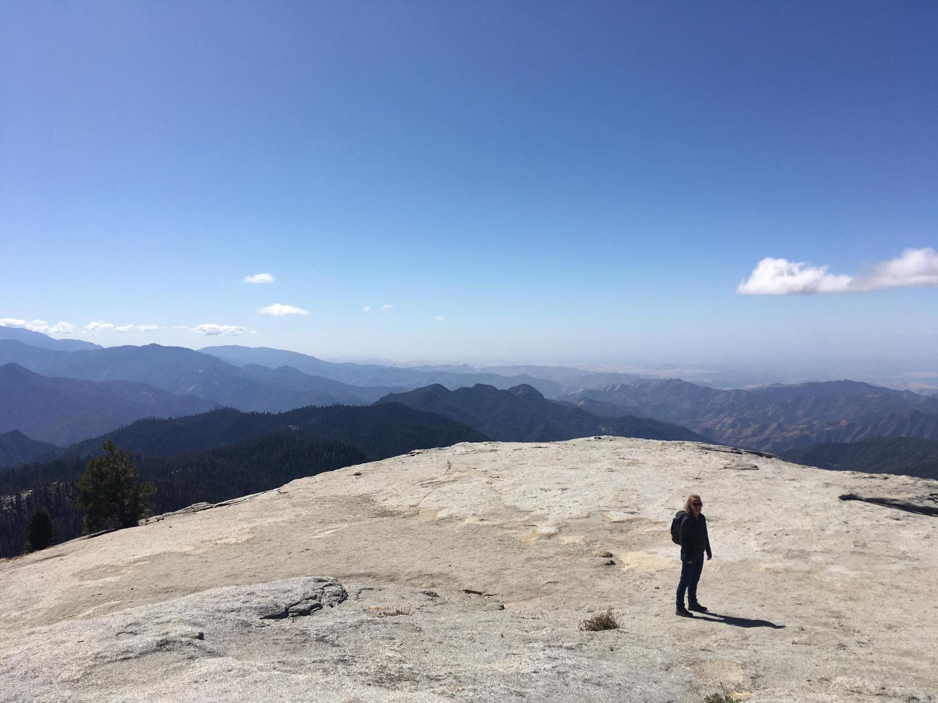A person stands on a rocky peak overlooking a vast mountain range.