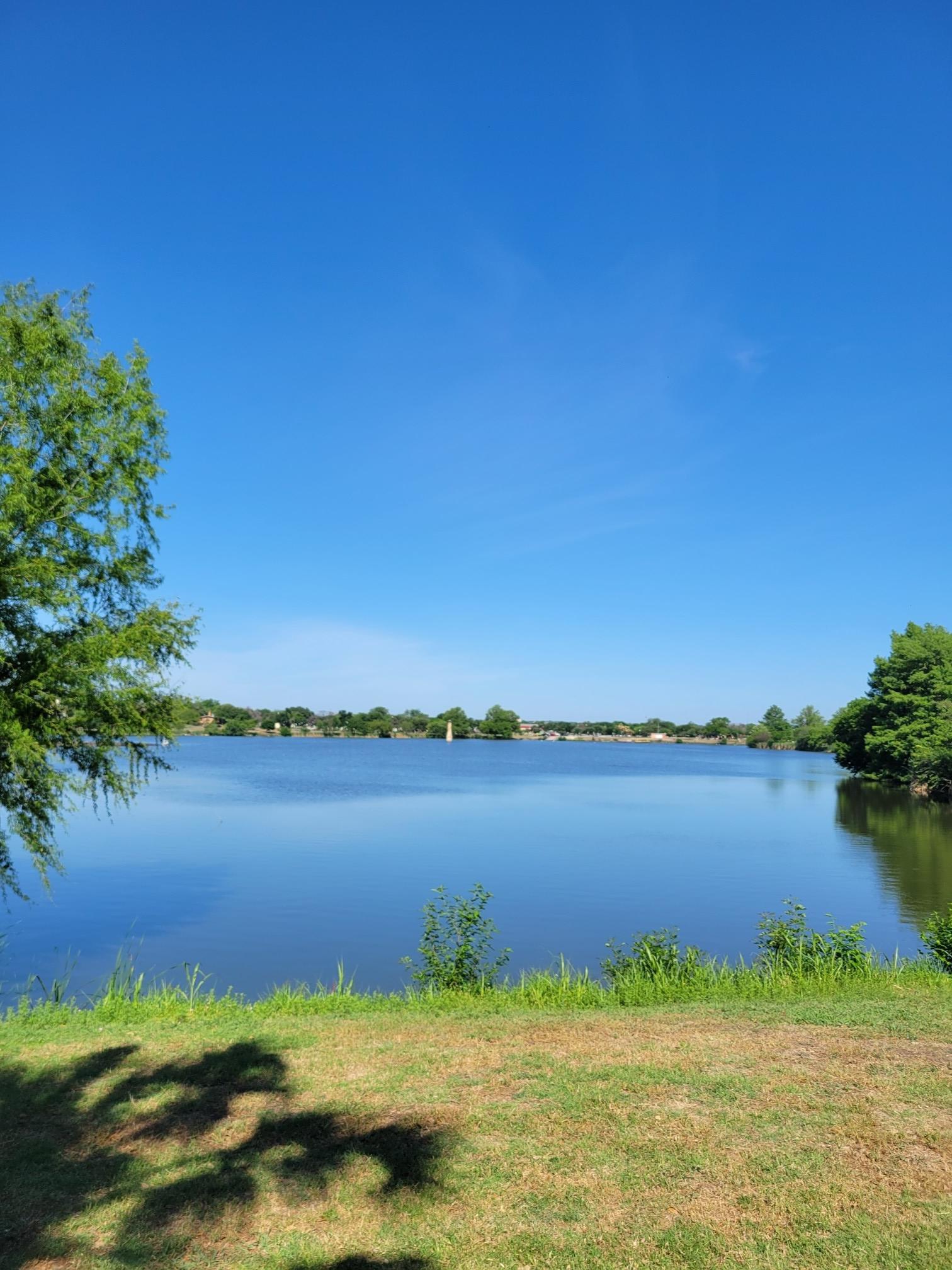 Sunny view of a calm lake with green shoreline and a clear blue sky.