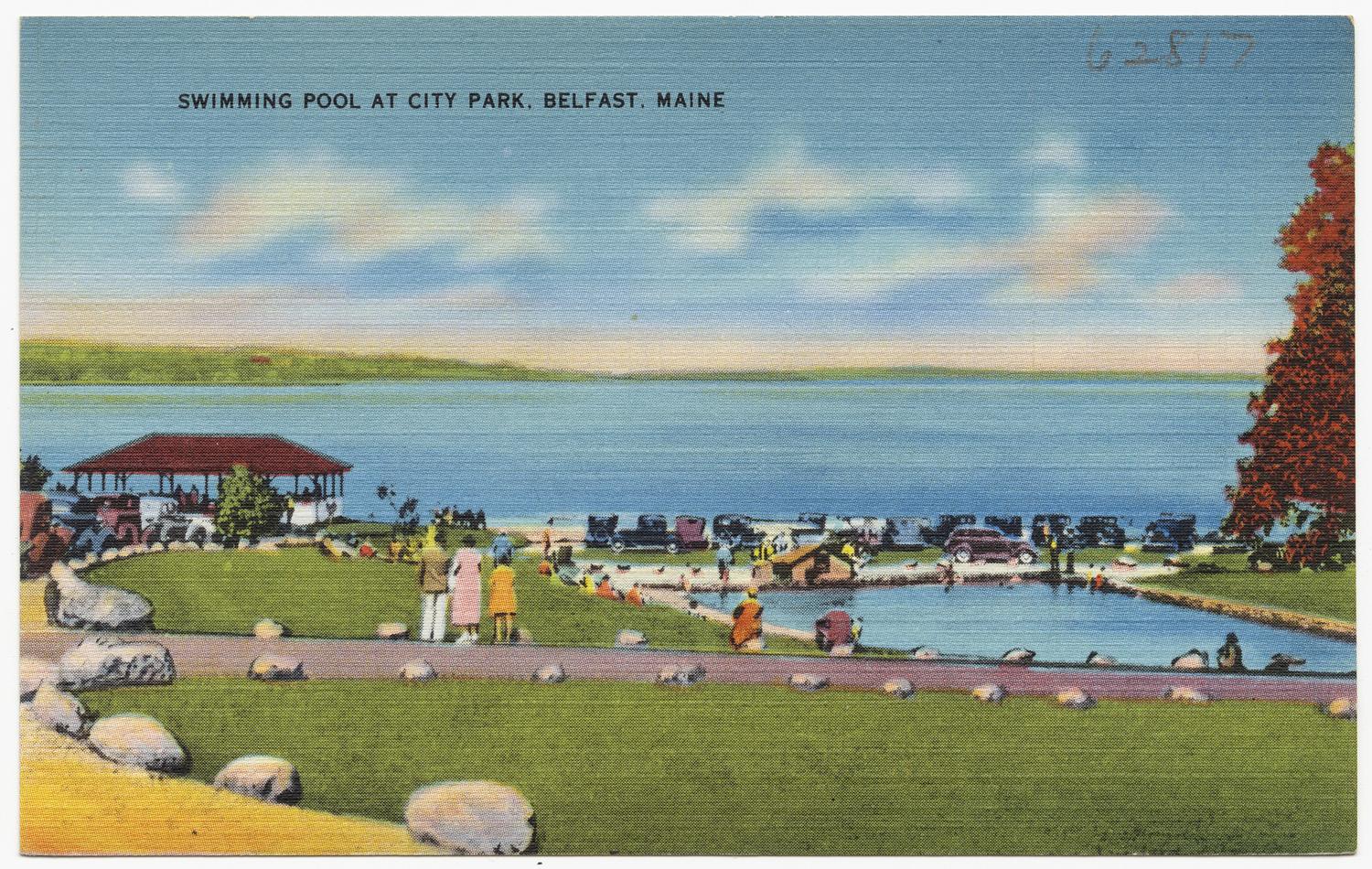 People gather around a swimming pool by a large lake on a sunny day.