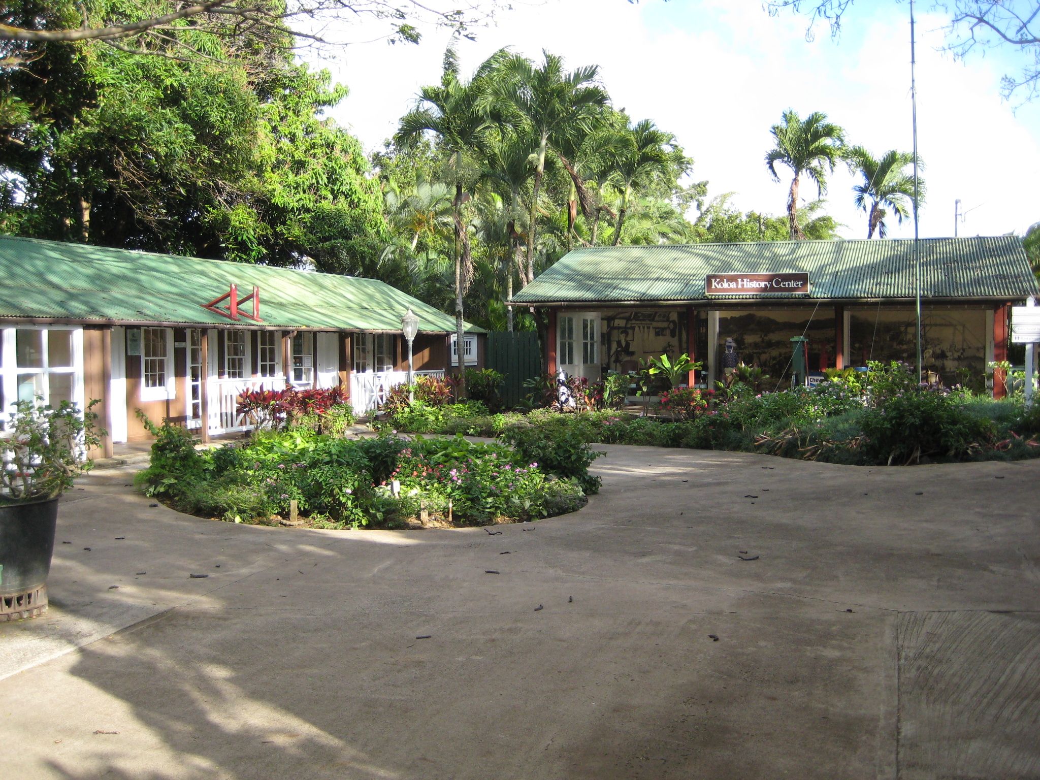 Two green-roofed buildings in a lush tropical garden under bright daylight. - Old Koloa Town via Poipu Road loop