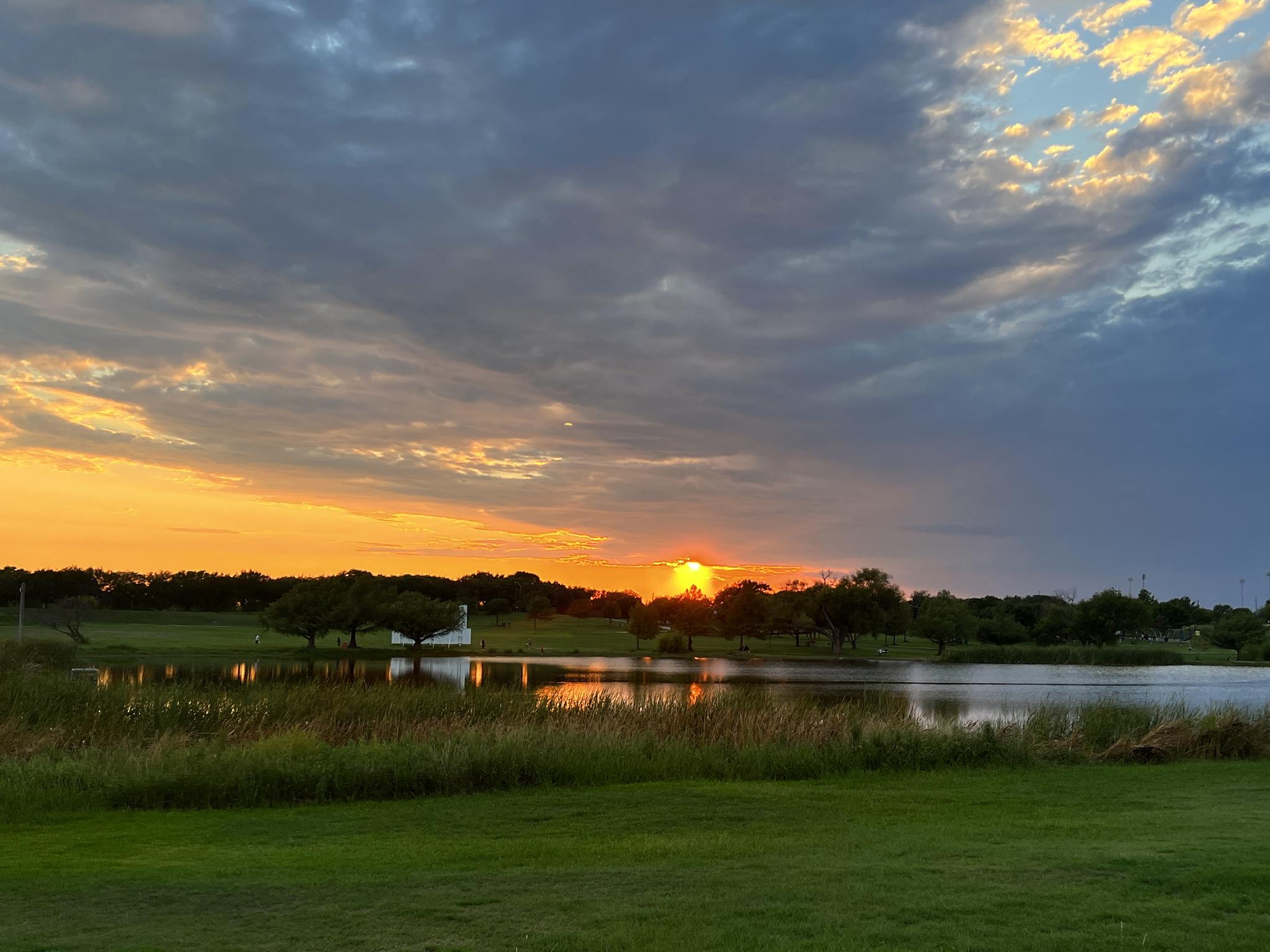 Golden sunset over a calm lake, reflecting vibrant sky colors and trees.