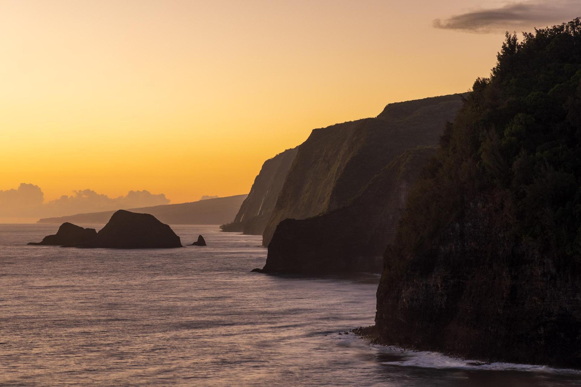 Dramatic sea cliffs and ocean at sunset, with warm orange light.