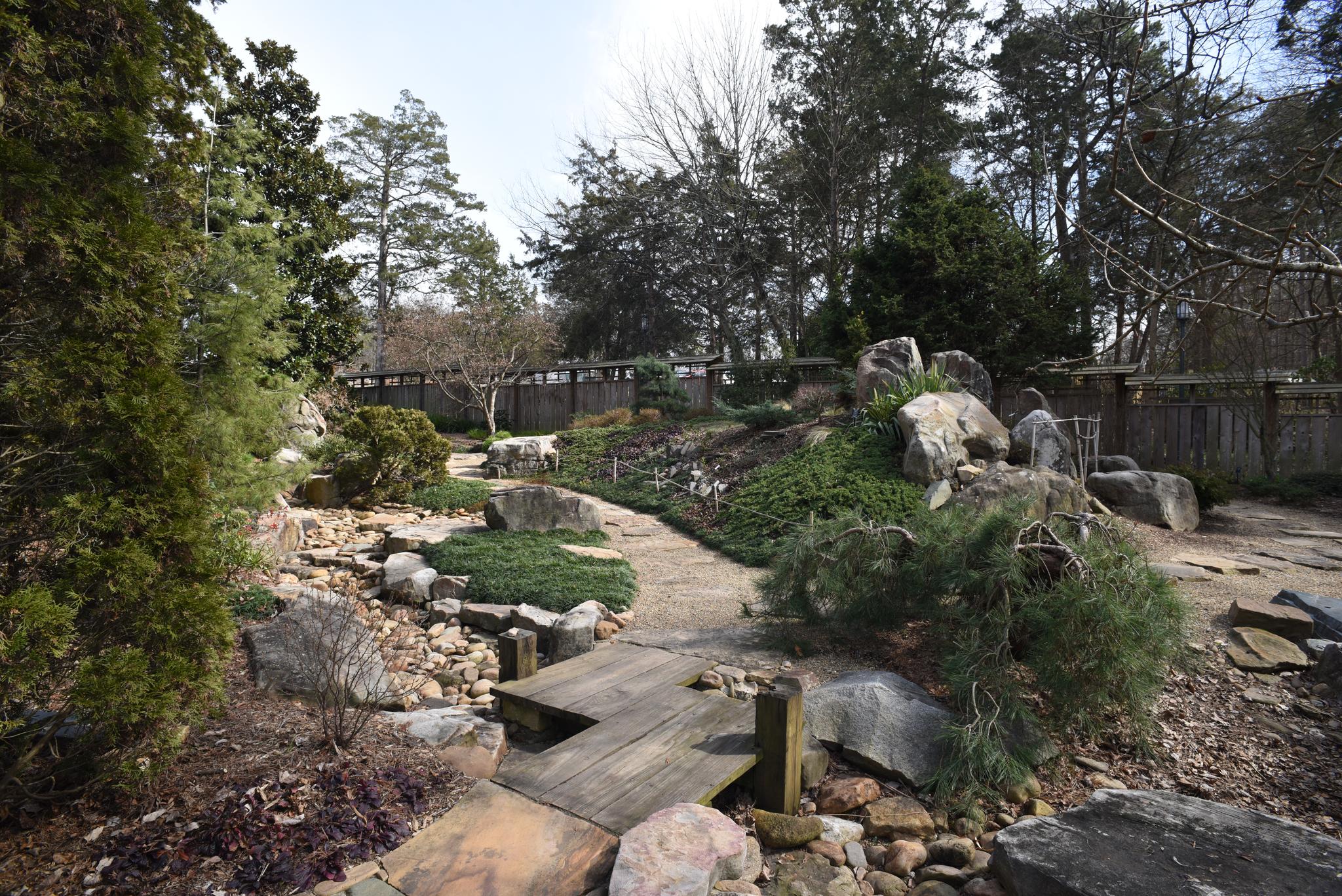 Rocky garden with a small wooden bridge and varied green foliage.