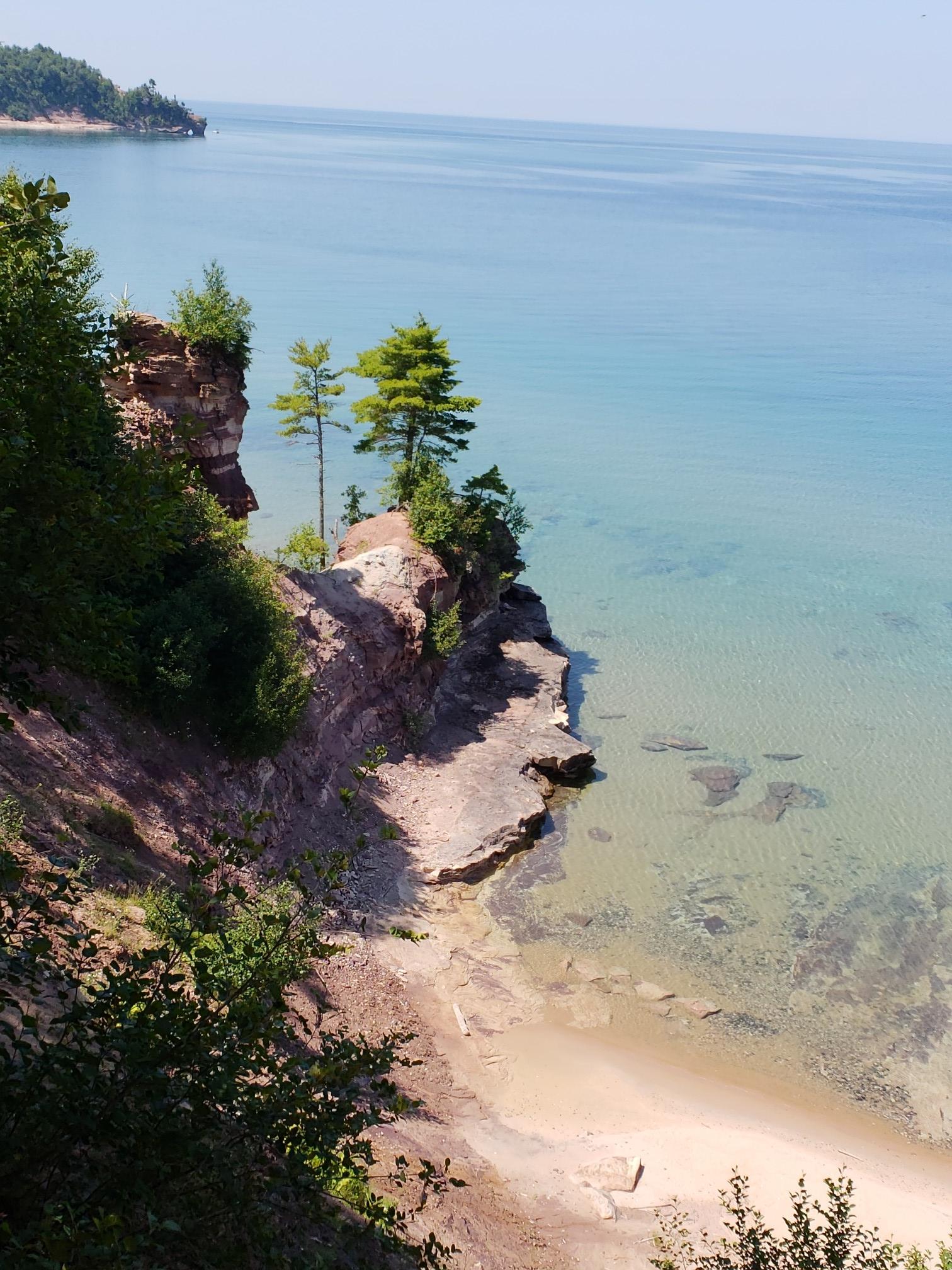 Clear blue water next to rocky cliffs and a sandy beach.