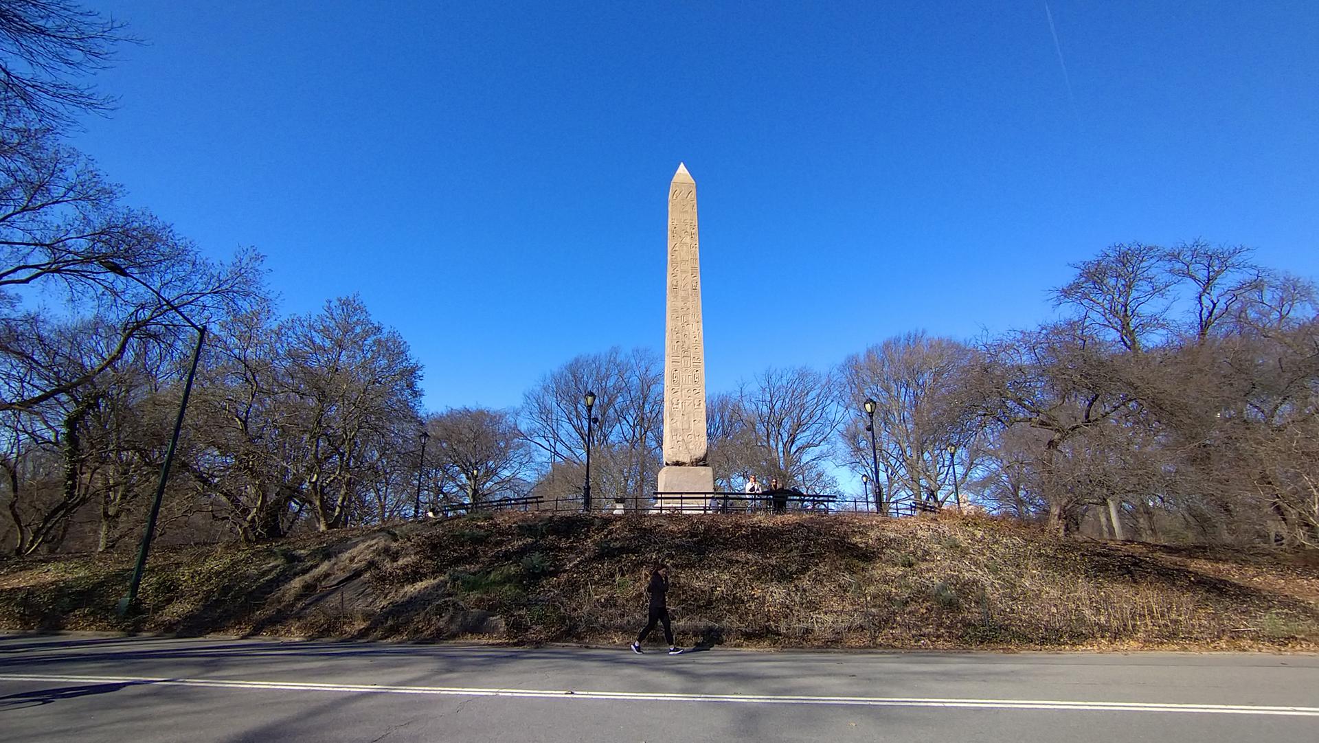 A tall obelisk monument stands on a grassy hill under a clear blue sky.