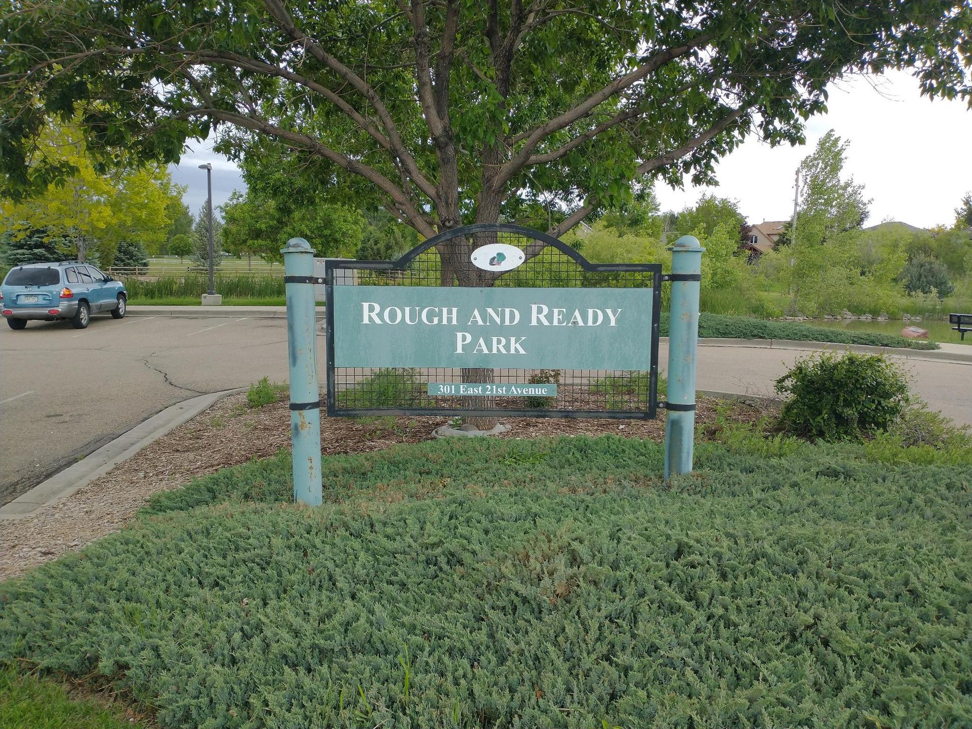 Green park sign surrounded by bushes, with a car and trees.