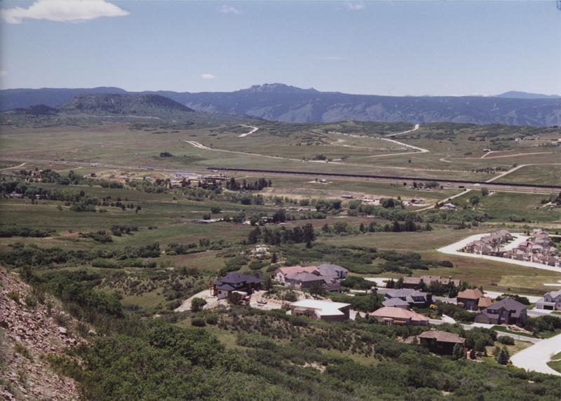 Vast hilly landscape with houses, winding roads, and distant mountains on a clear day.