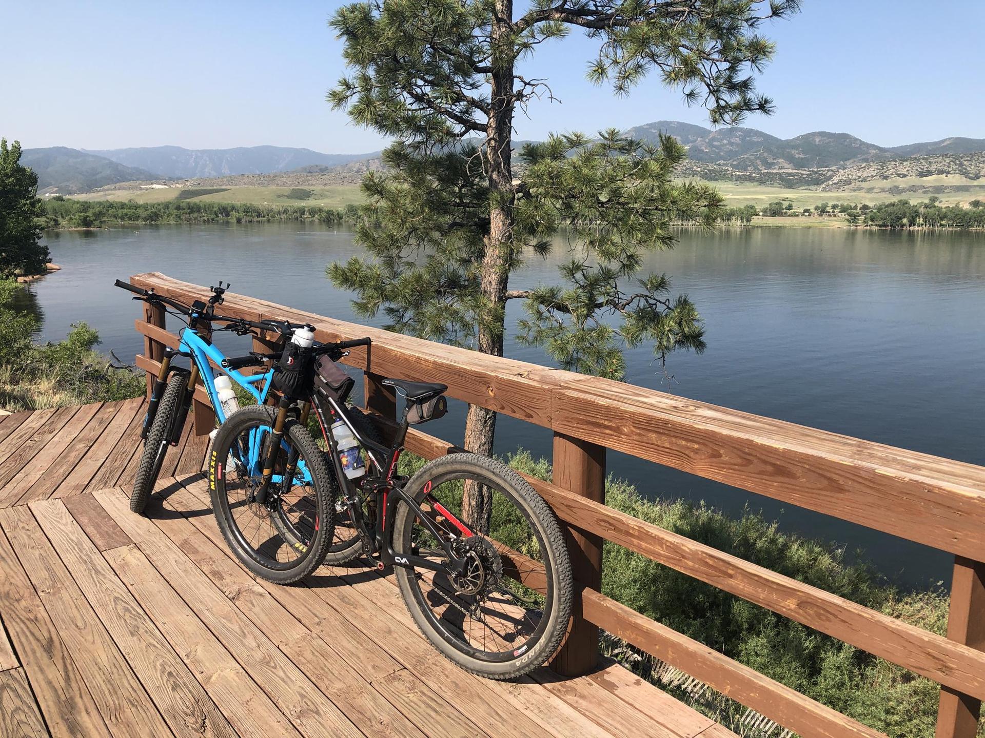 Two mountain bikes rest on a wooden deck overlooking a serene lake and mountains.