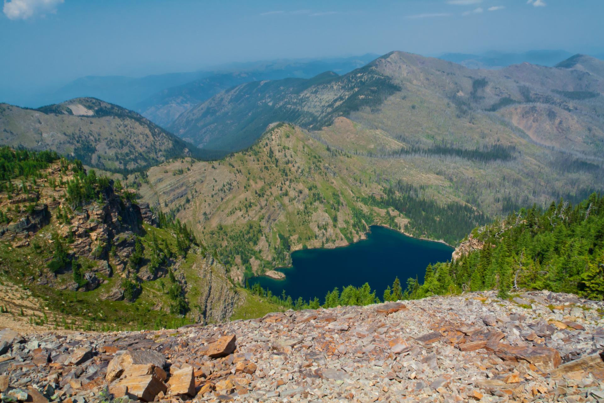 An aerial view of a deep blue lake nestled among vast, rugged mountains.