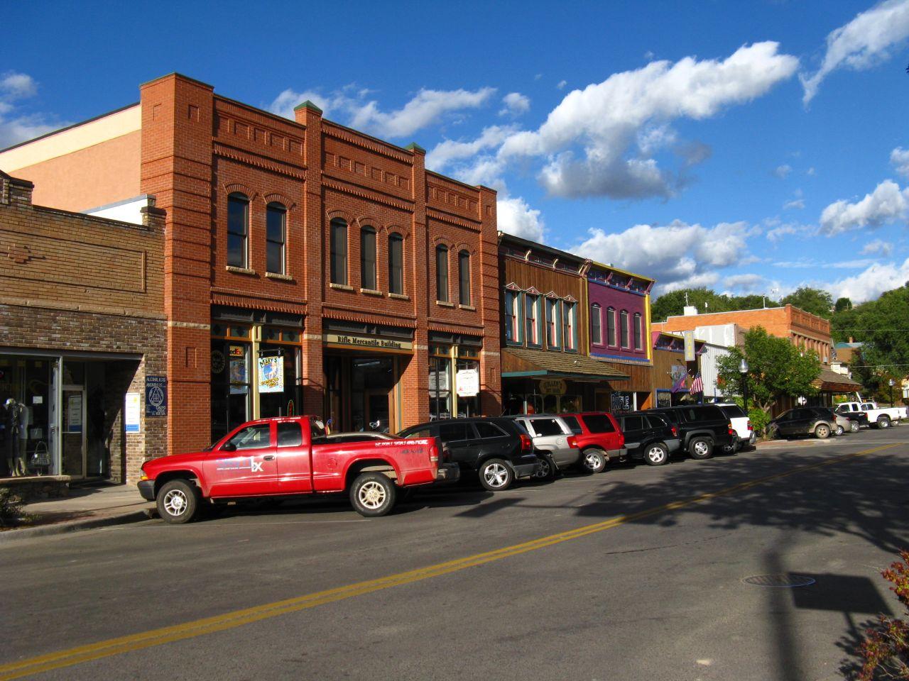 Historic brick buildings line a sunny street with parked cars.