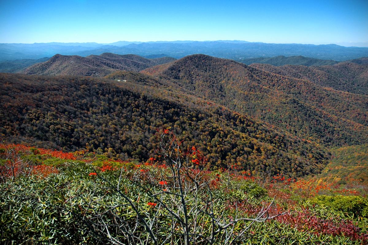 Vast mountain range with autumn foliage under a clear blue sky.