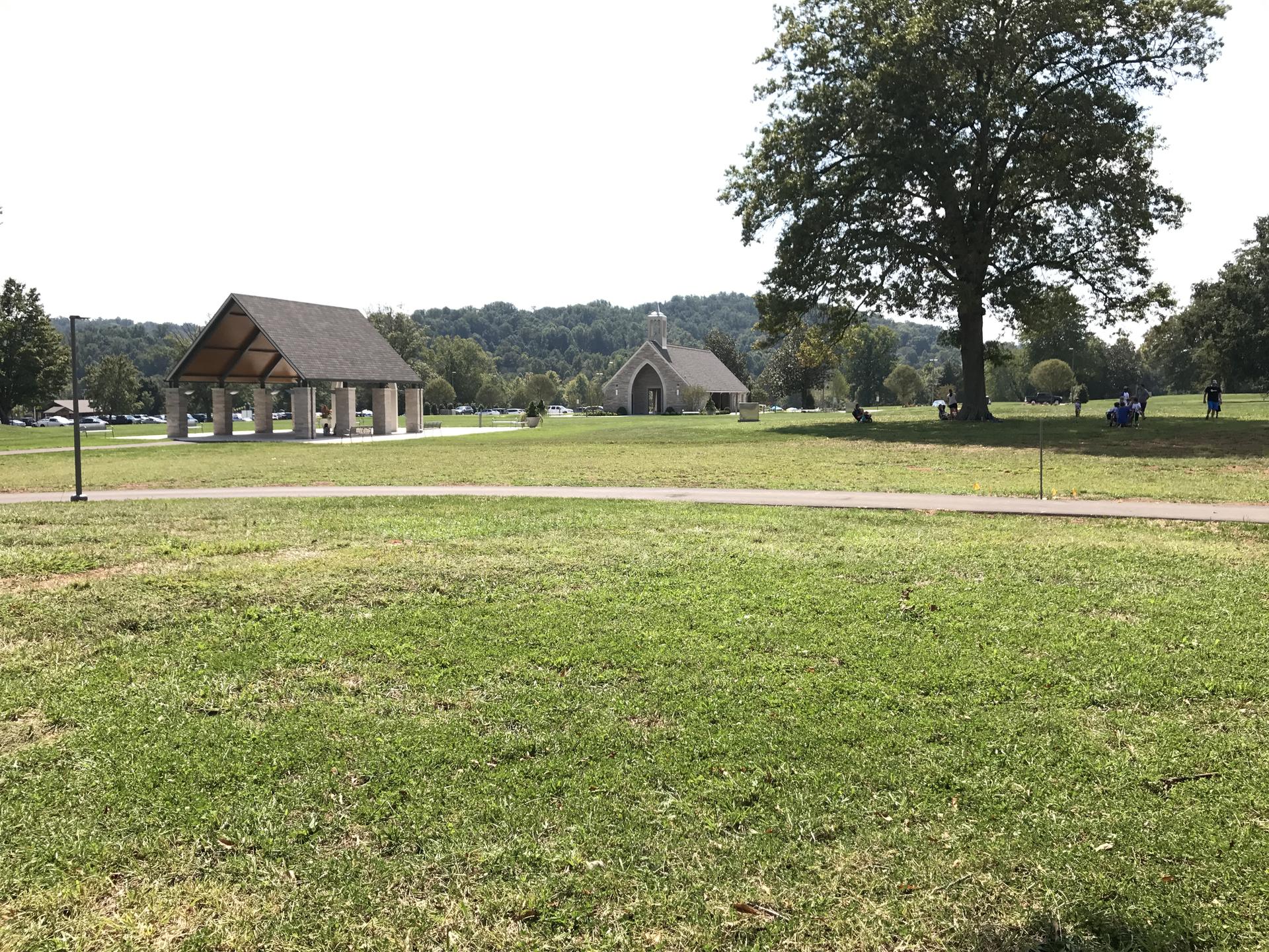 Sunny day over a large grassy field with a pavilion and distant building.