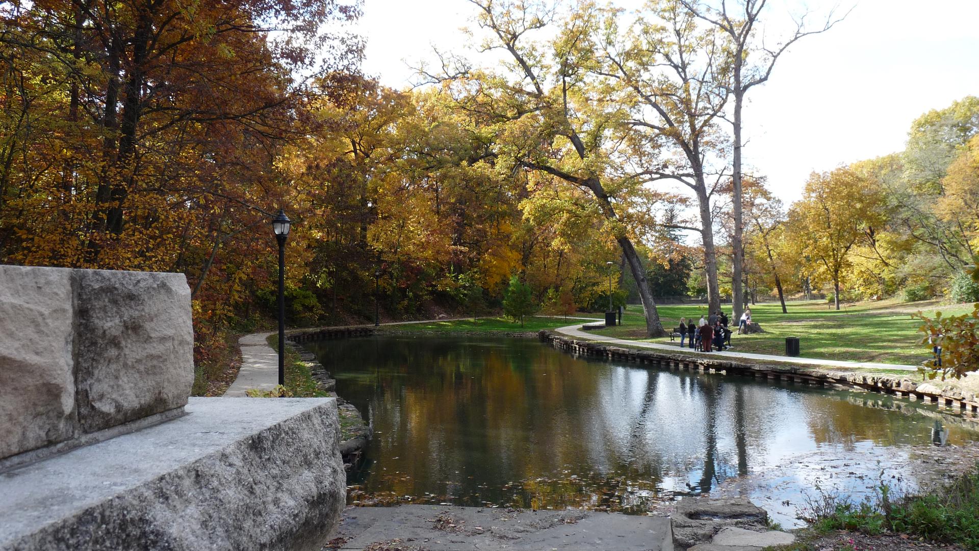 Bright autumn day with a path, calm water, colorful trees, and a group of people.