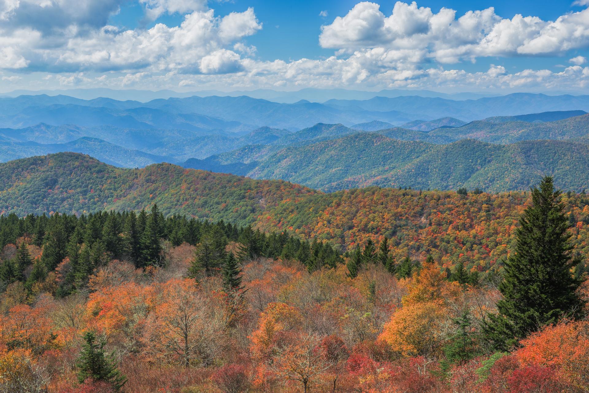 Expansive mountain landscape with colorful autumn trees under a partly cloudy sky.