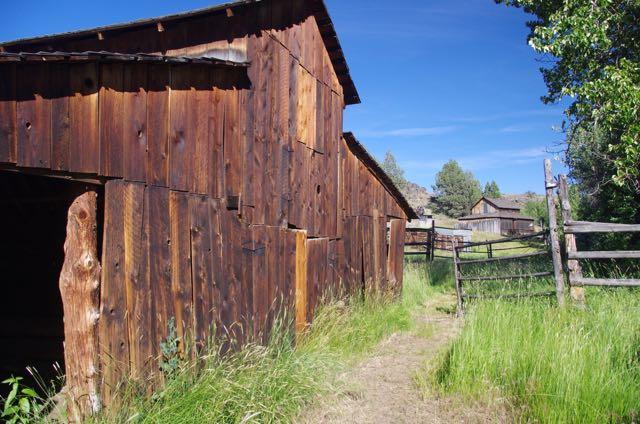 Weathered wooden barn next to a dirt path and fence on a sunny day.