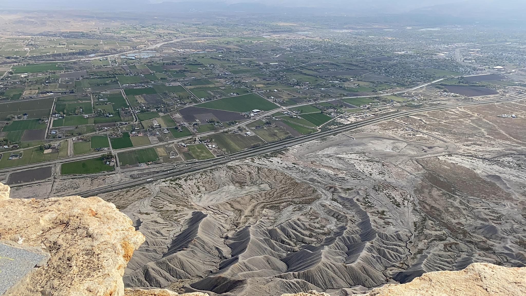 High angle view of cultivated fields, roads, and eroded badlands from a cliff. - Mount Garfield Trail