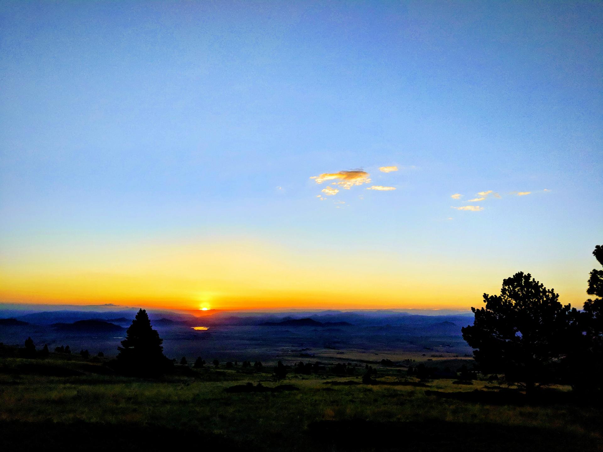 Golden sunset over a vast landscape with silhouetted trees and distant hills.