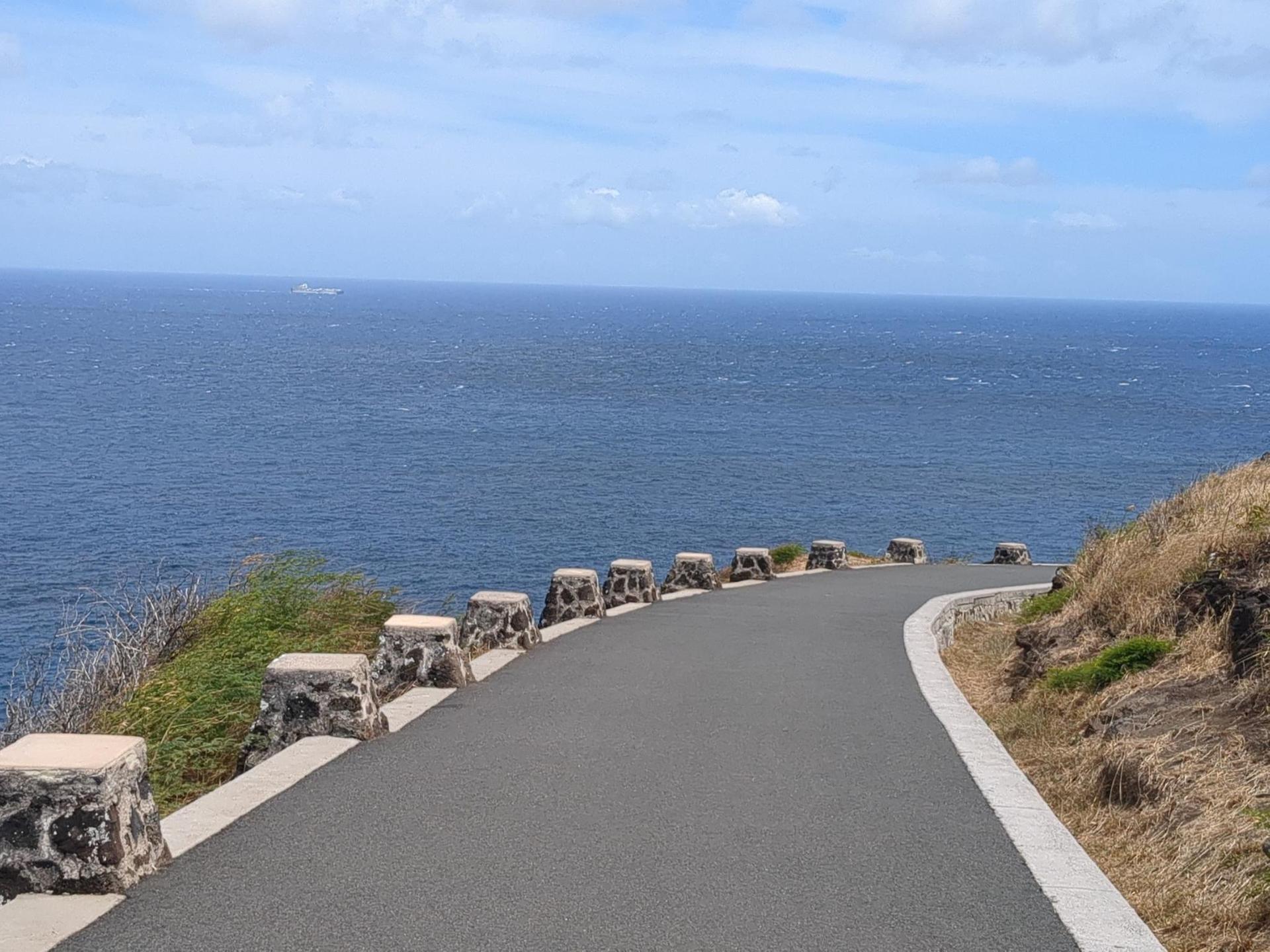 Paved road with stone barriers curving along a cliff overlooking a vast blue ocean.