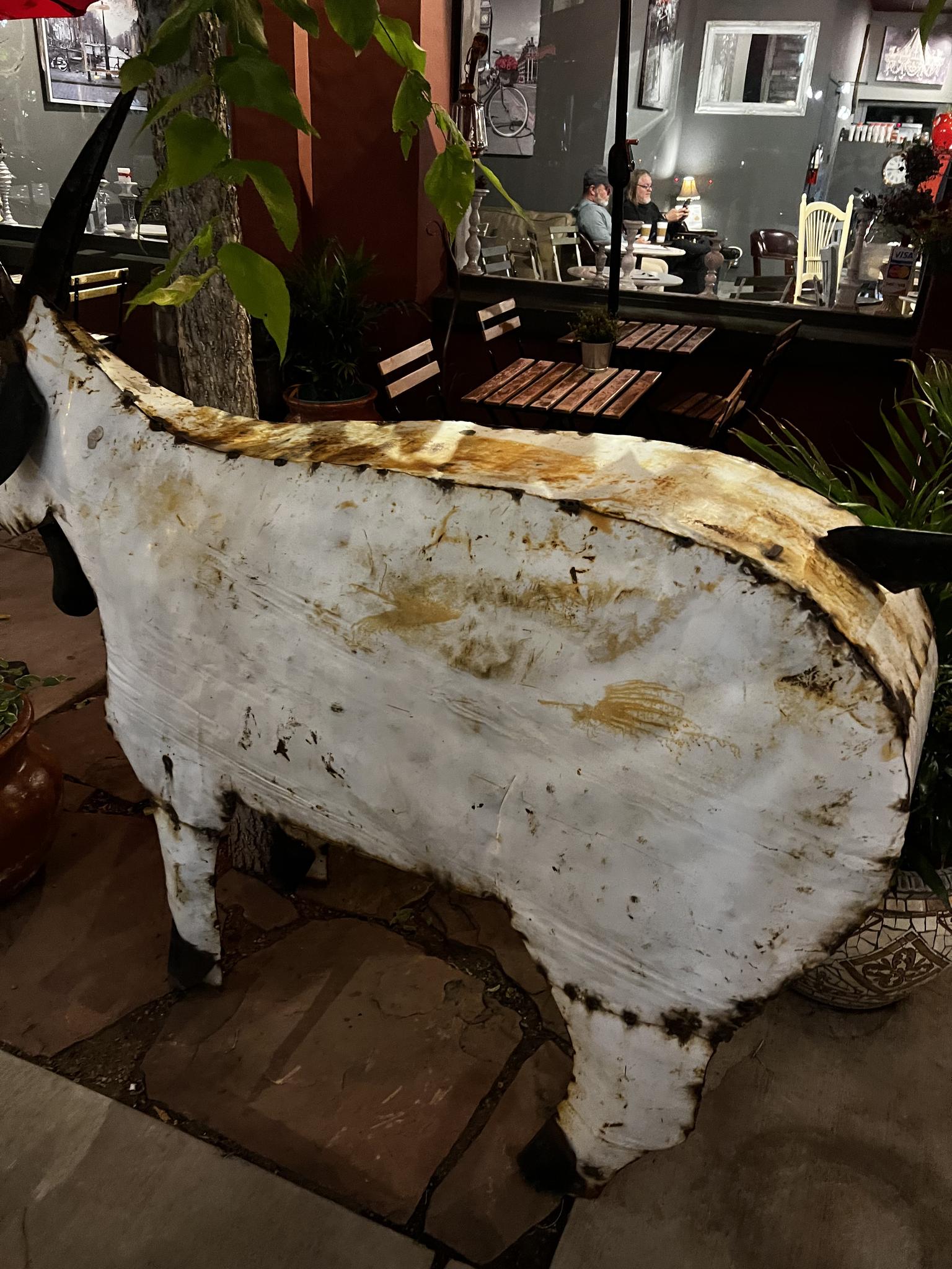 Weathered white animal sculpture on a patio with blurred tables and chairs.