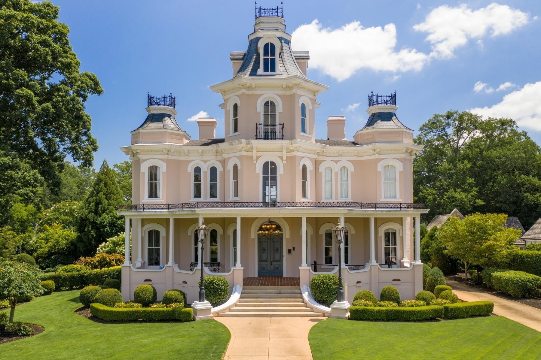 Grand, ornate mansion with a manicured lawn under a bright, partly cloudy sky.