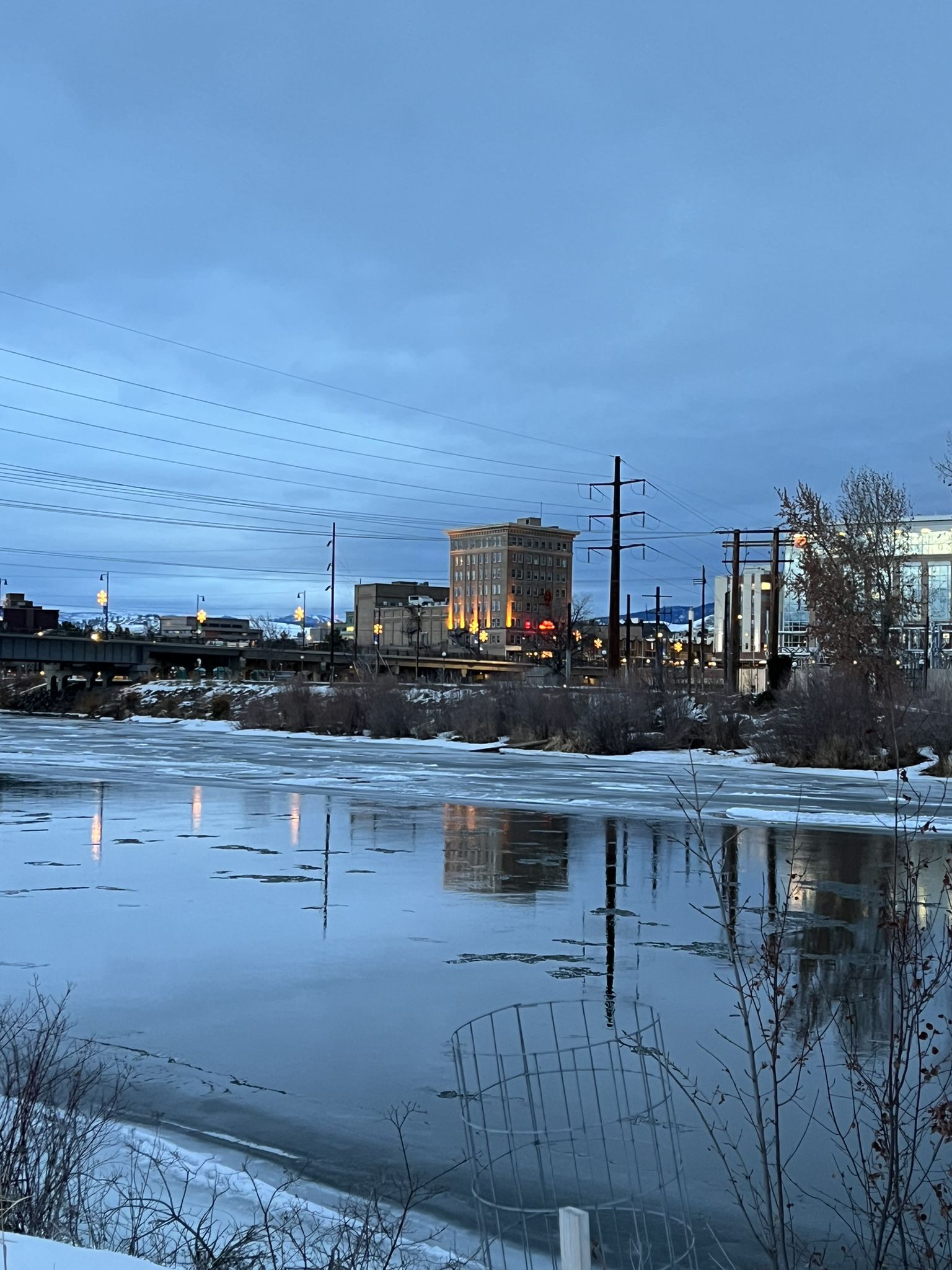 An icy river reflects city lights under a blue twilight sky. - Clark Fork River – Kim Williams Trail loop from Ogren Park at Allegiance Field