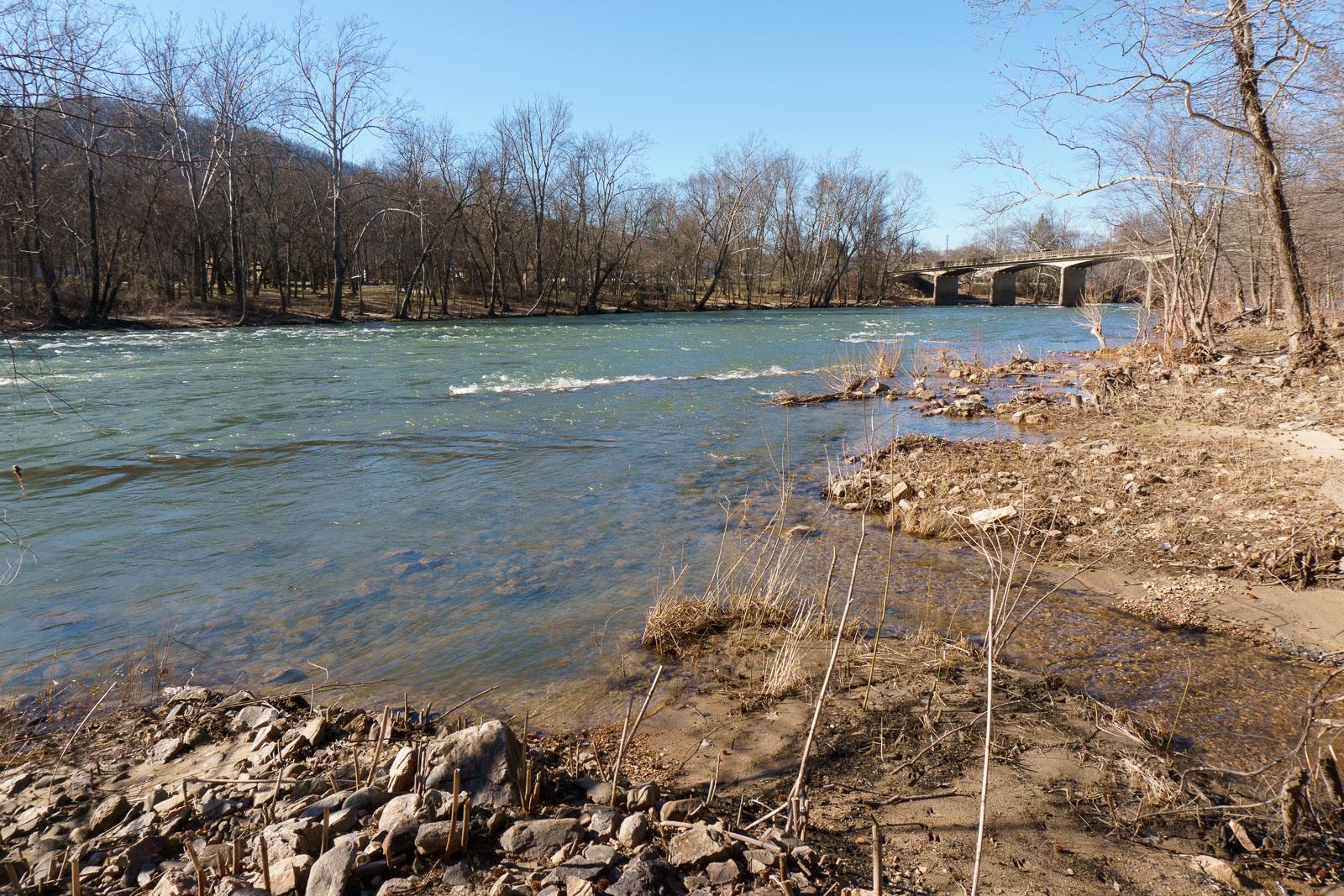 A wide river flows past a rocky bank under a clear sky.