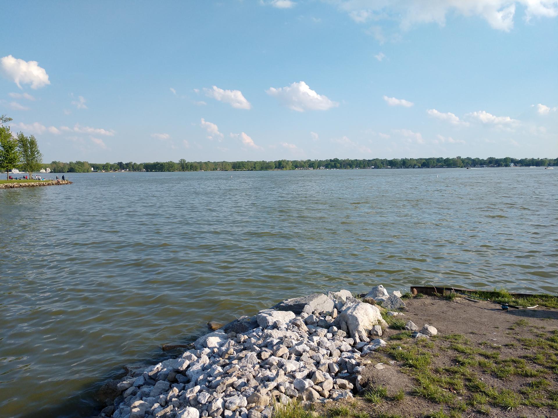 Sunny day over a wide lake with distant trees and people on a dock.