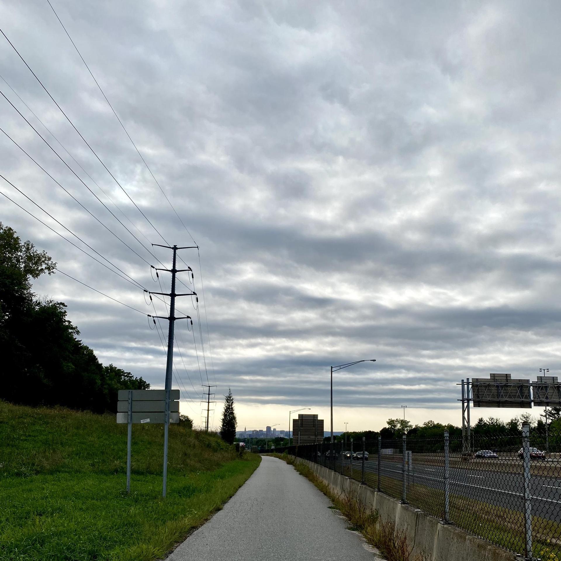 A paved path runs alongside a highway under a cloudy, overcast sky.
