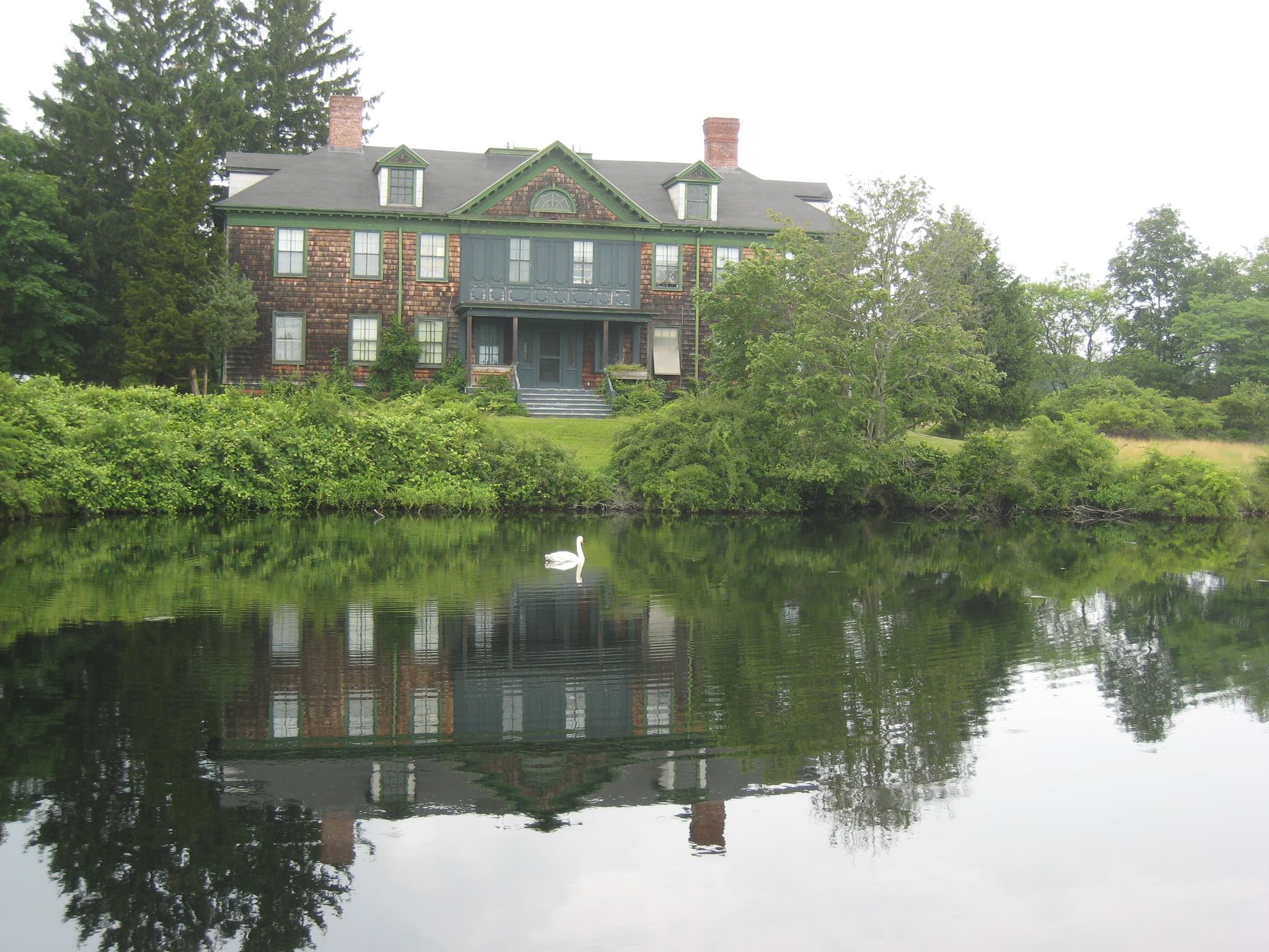 Large historic house reflected in a calm lake with a white swan.