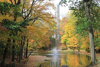 Autumn trees with colorful leaves surround a pond with a central water fountain.