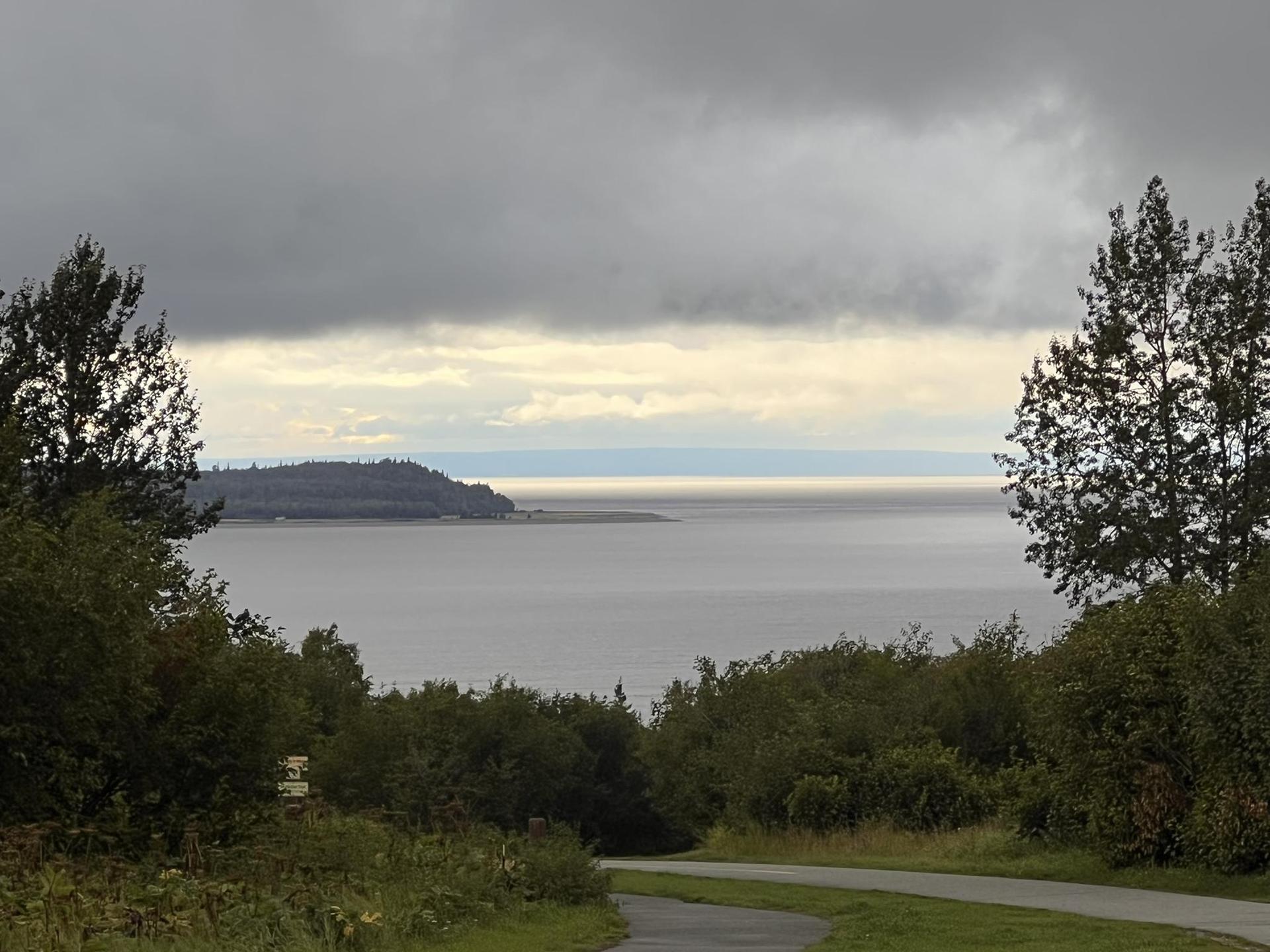 Paved road descends towards a wide body of water under a dark sky.