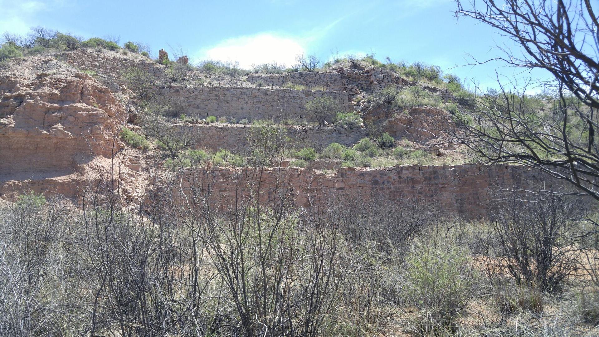 Dry, rocky hillside with terraced levels and sparse vegetation under bright sun.